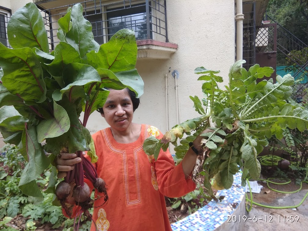 A participant proudly holds a fresh harvest of beetroot and radishes grown in Anugraha's garden