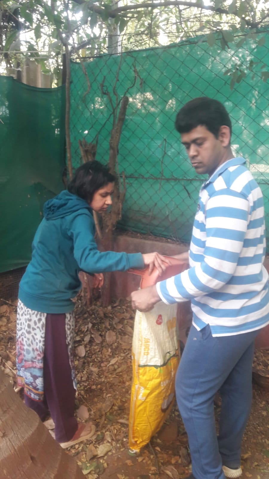 A participant in an orange t-shirt sweeps the floor and collects debris neatly into a dustbin
