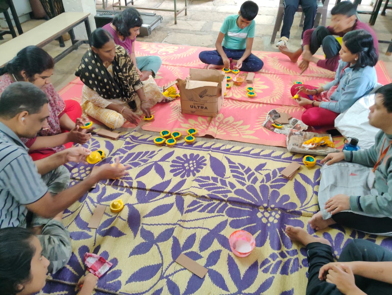 Group seated on floor painting diyas