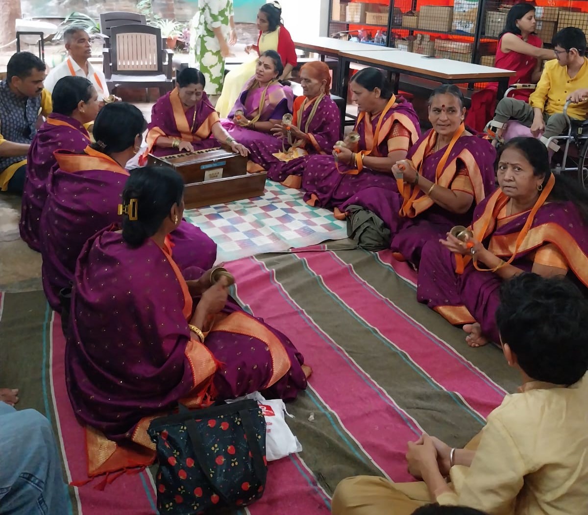 Women in traditional attire singing with harmonium and cymbals